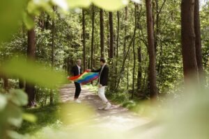 Gay couple celebrating with a rainbow flag in a vibrant forest setting.
