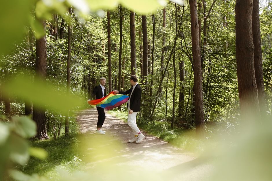 Gay couple celebrating with a rainbow flag in a vibrant forest setting.